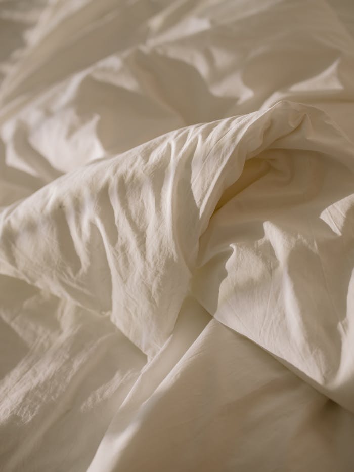 gallery-3 Close-up of crumpled white bed linen with soft natural lighting, evoking coziness.