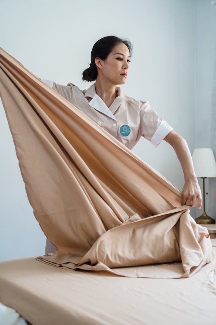 A hotel staff member expertly makes a bed, showcasing efficiency and attention to detail.